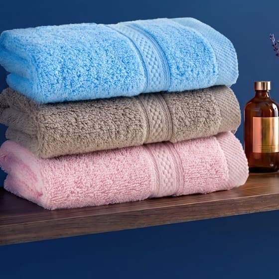 Ba chiếc khăn mặt Toweland màu xanh dương, ghi và hồng trên kệ gỗ nền xanh navy.